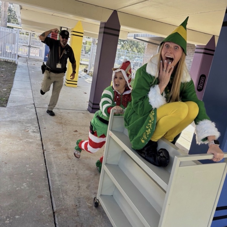 two teachers dressed as elves being chased around a school campus for a fun photo