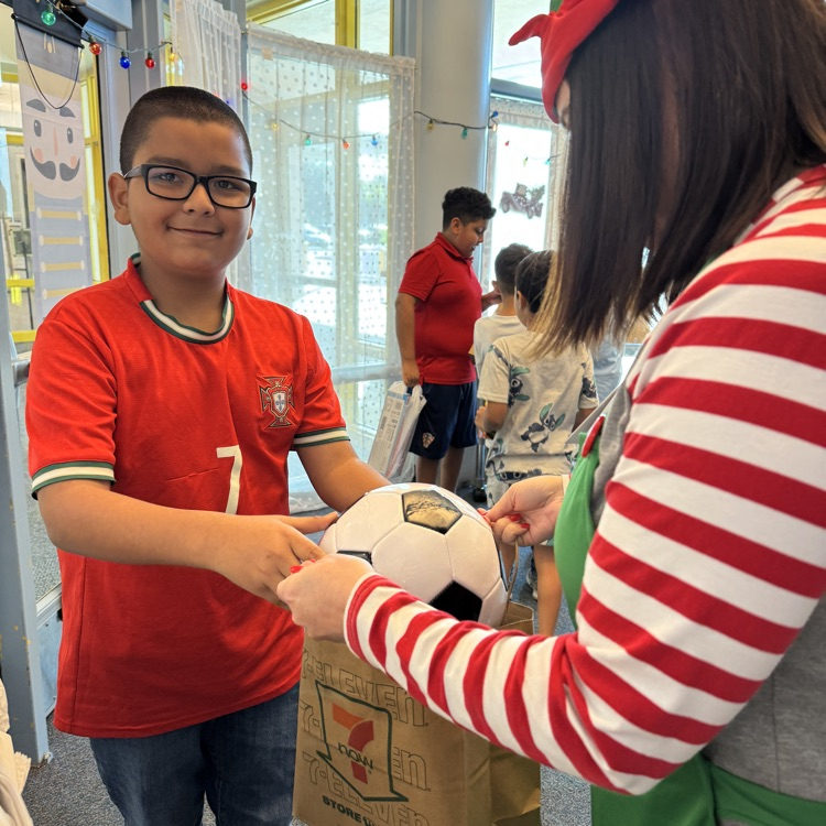 teachers help a child put a toy from Santa’s workshop in a bag