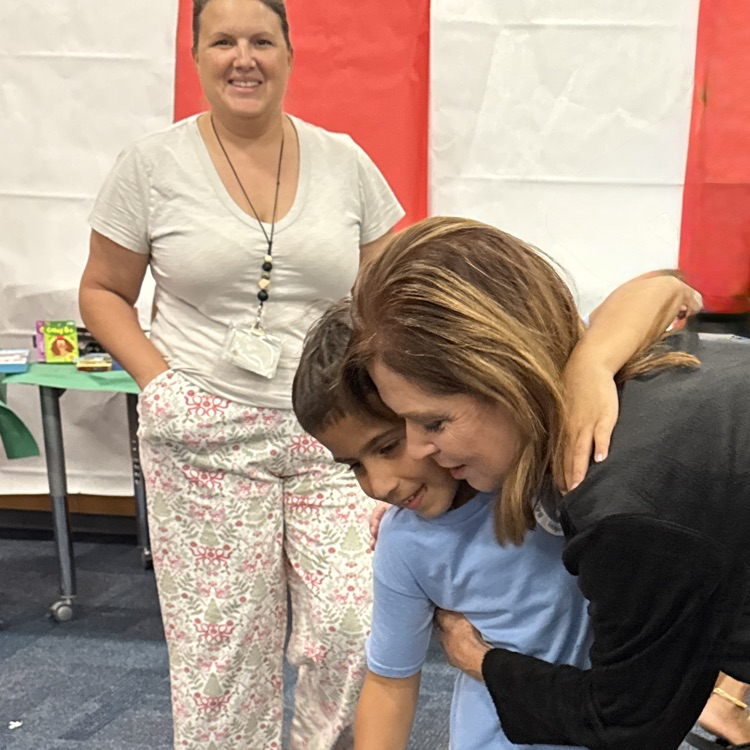 A child hugged the school principal with a teacher, smiling in the background