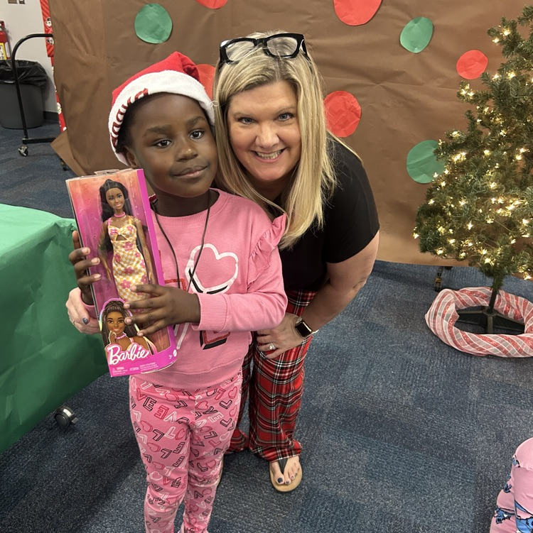 The assistant principal smiles next to a young girl who’s picked out a Barbie for Christmas
