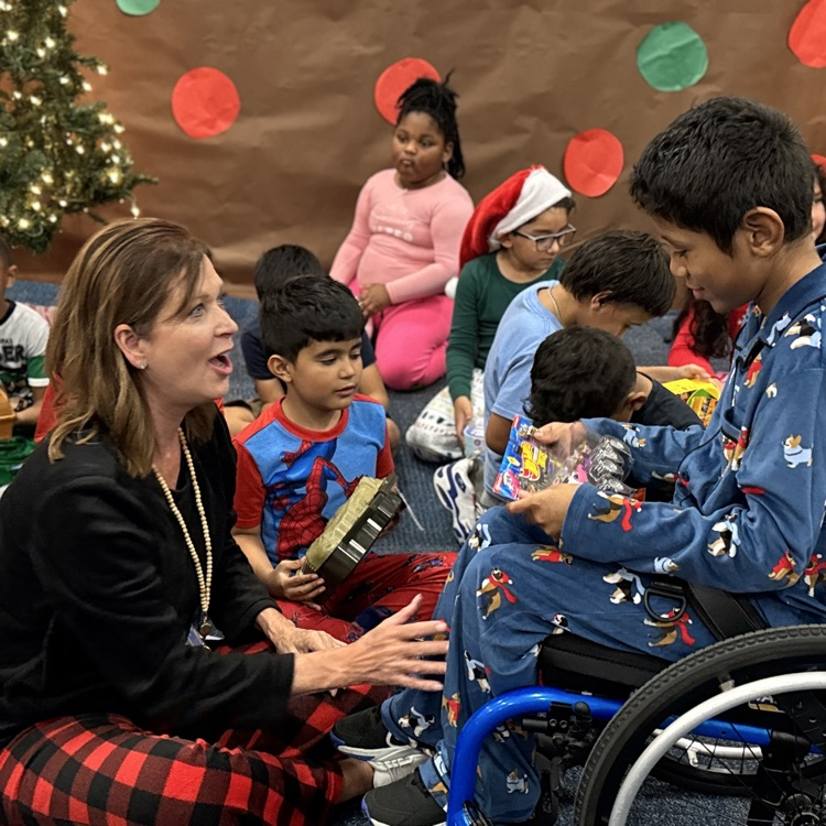 The principal sitting on the ground smiling at a young boy in a wheelchair