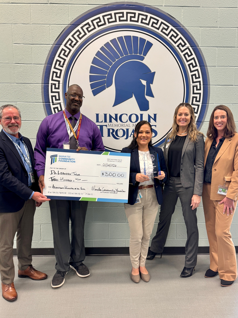 School and community leaders holding a large check and standing by a large sign that reads, Lincoln Trojans.