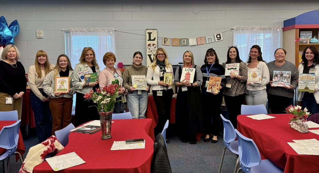 A line of women holding books up and smiling in a school media center.
