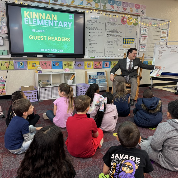 A guest reader smiling as he reads to a classroom