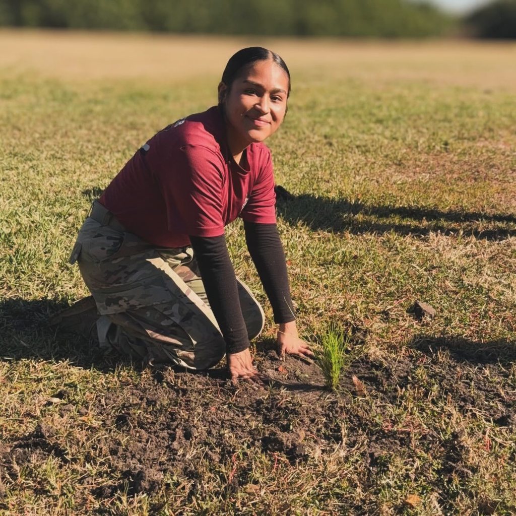 JROTC student kneels down with a freshly planted pine sapling.