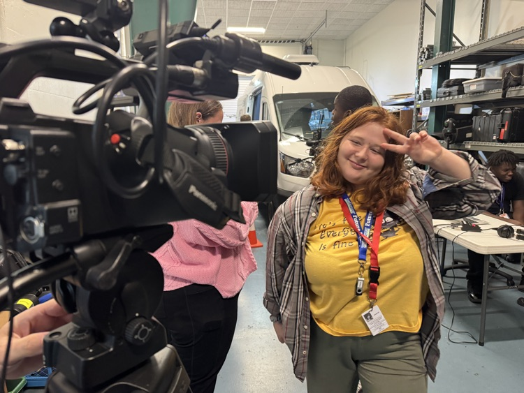 A student gives a peace sign in front of a television camera
