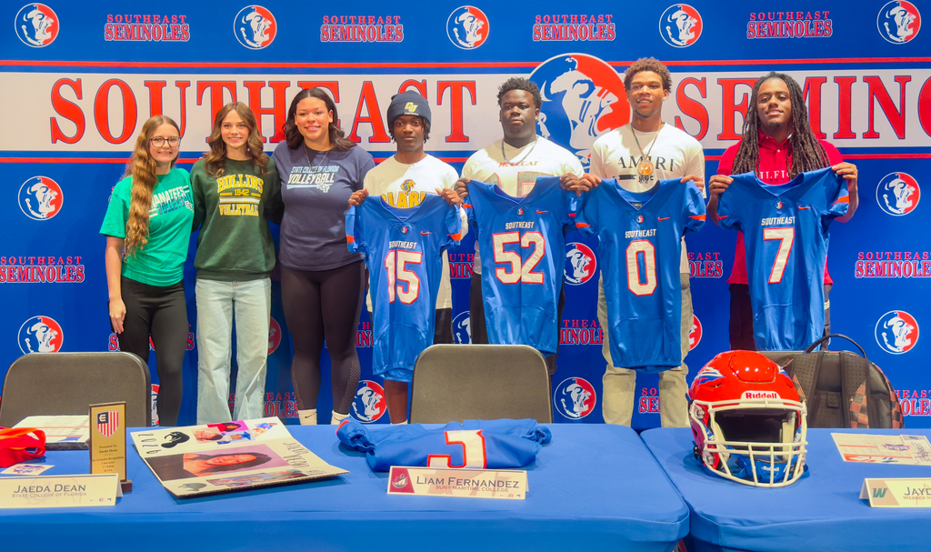 High school athletes hold up their jerseys and stand together in celebration of college signing day.