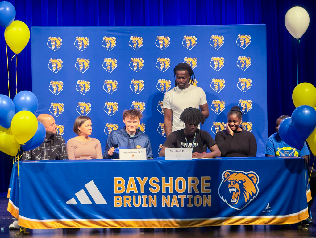 Signing day at Bayshore High with a school backdrop featuring yellow and blue.