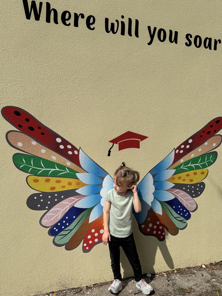 A child standing next to a mural with butterfly wings
