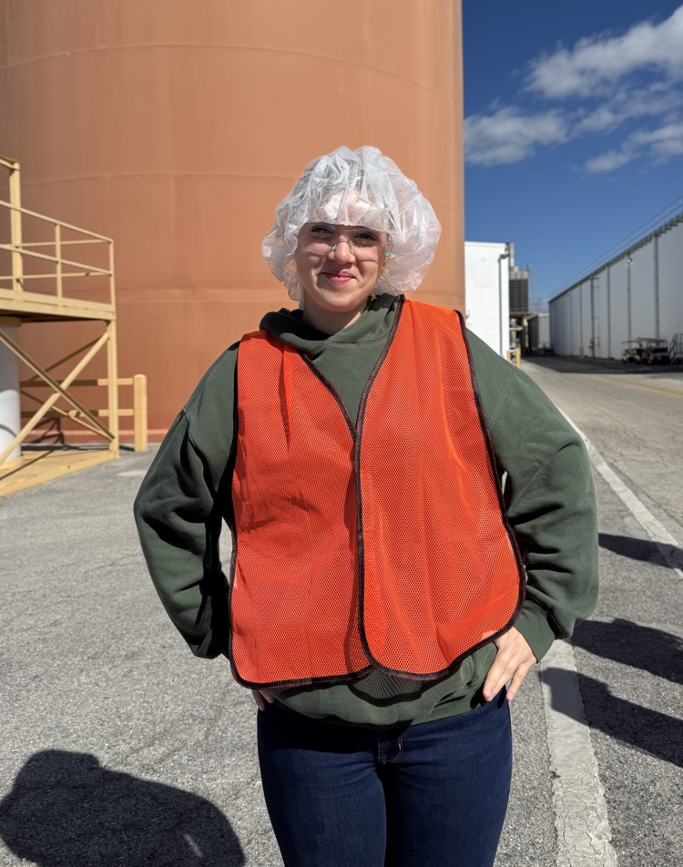A young woman wearing a safety vest and hairnet at a manufacturing plant