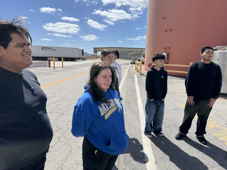 Students gathered outside of manufacturing plant for a field trip, smiling