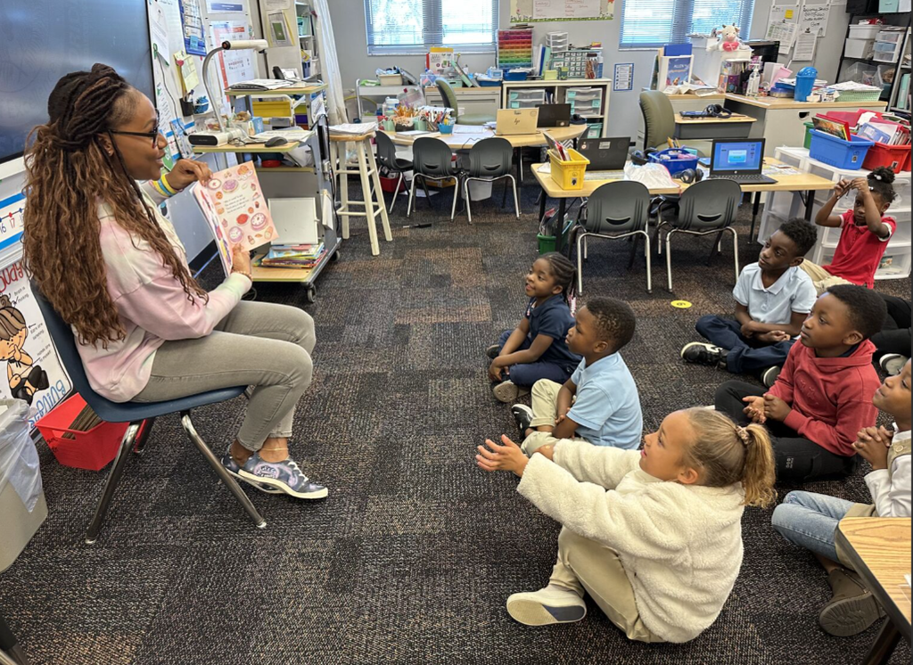 Children smiling while listening to a guest author read a book in their classroom.
