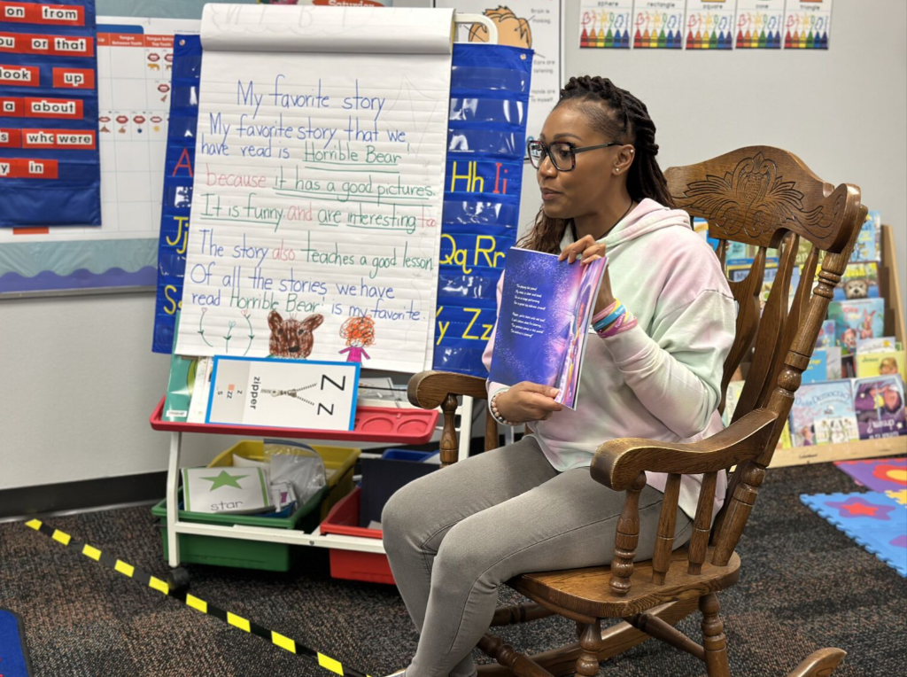A guest author holding up a book while sitting in a rocking chair.