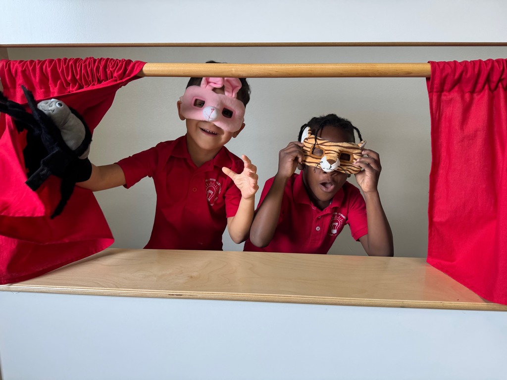 Two young kids wearing masks play in a puppet theater.