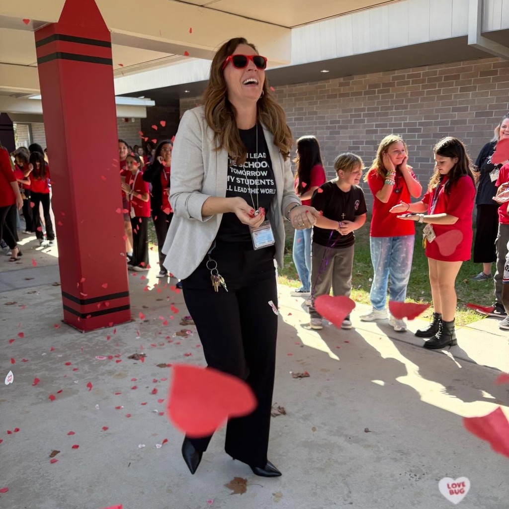 A school principal laughs as students clap and throw heart shaped confetti at her as a means of goodbye.