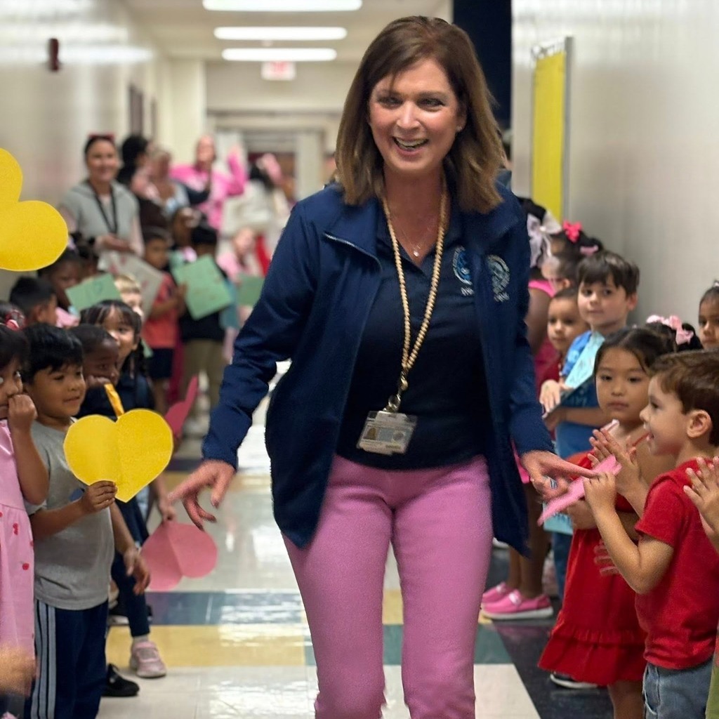 a school principal gives high fives through a school hallway with children clapping.