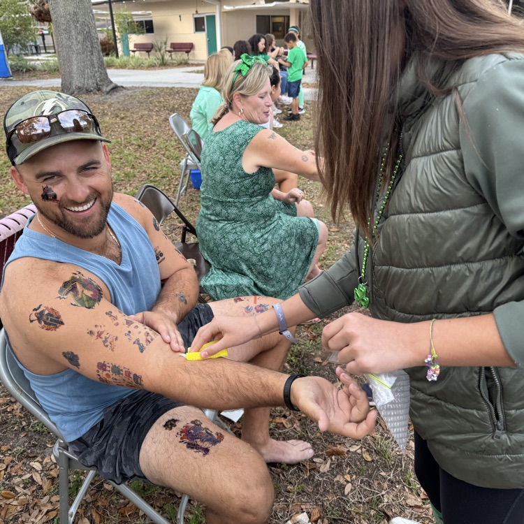 A man laughs as students surround him while holding temporary tattoos
