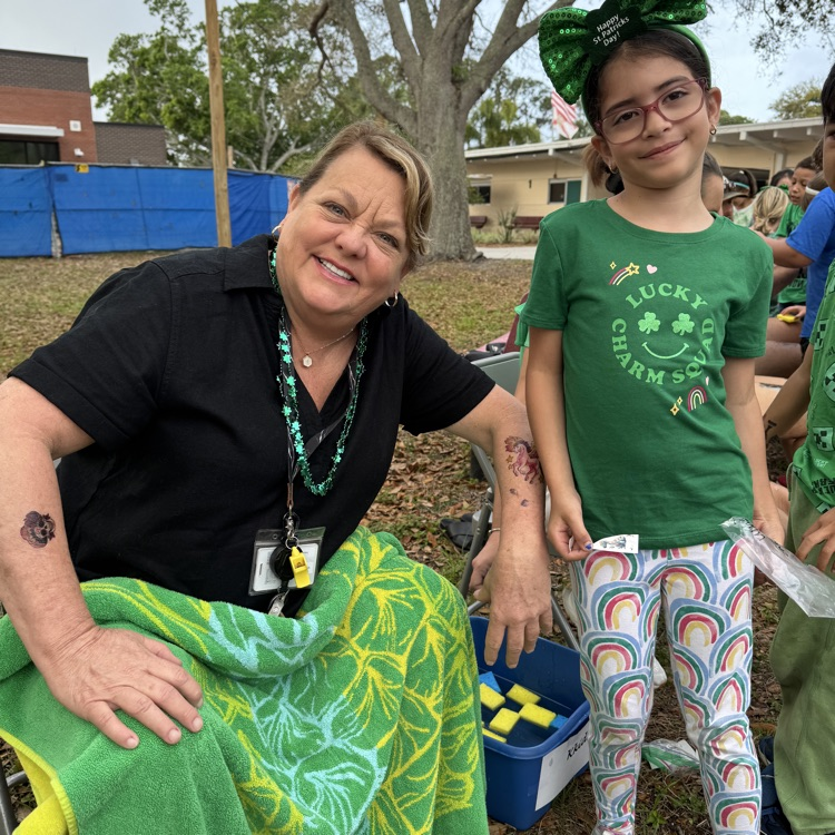 A teacher and student wearing green smile for the camera