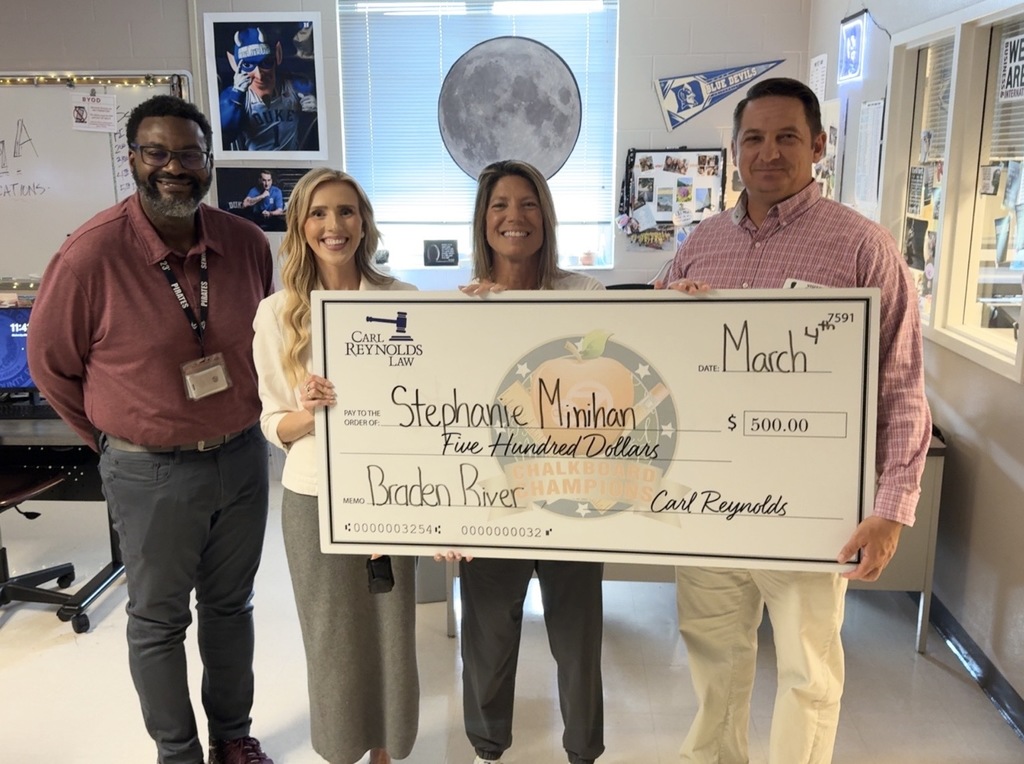 Four adults smiling while a teacher holds a giant check for $500.