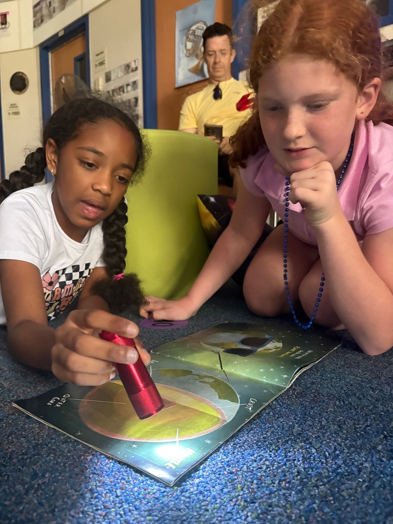 Students holding a flashlight up to a book about science.