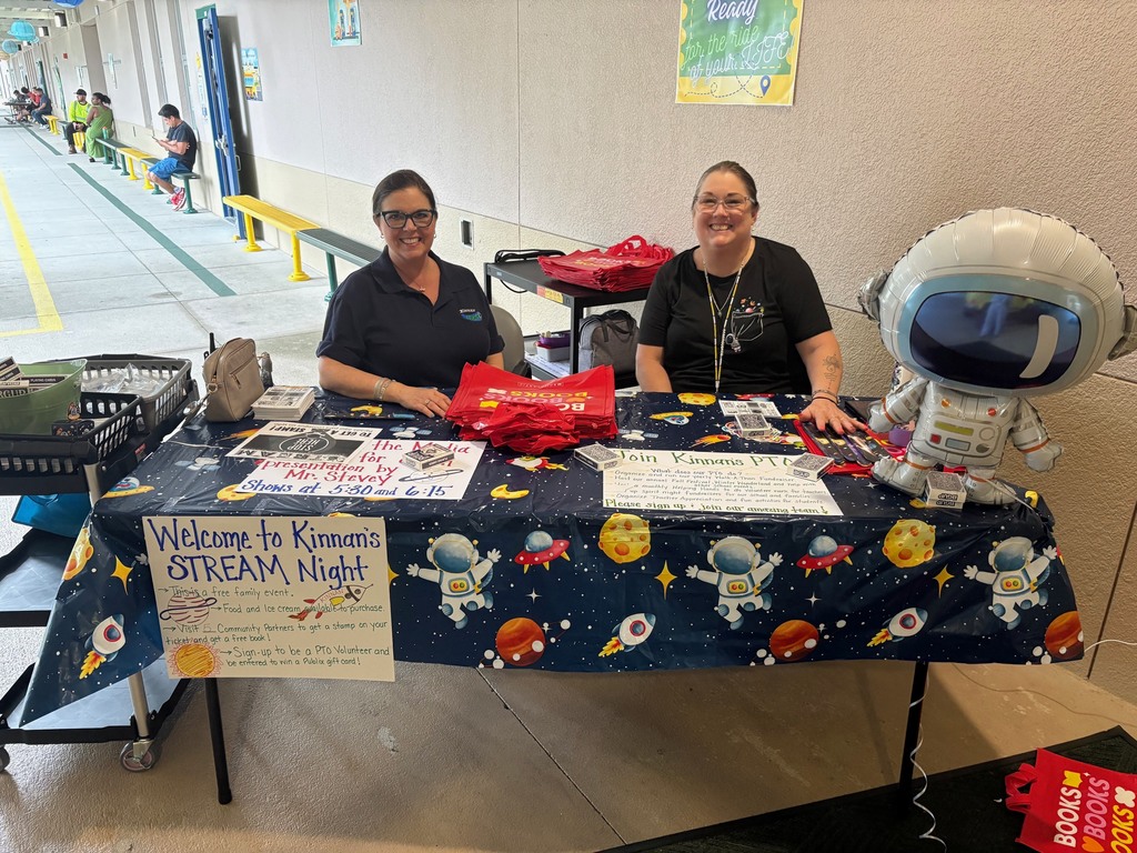 Two educators sitting at a space themed table welcoming families to STREAM Night