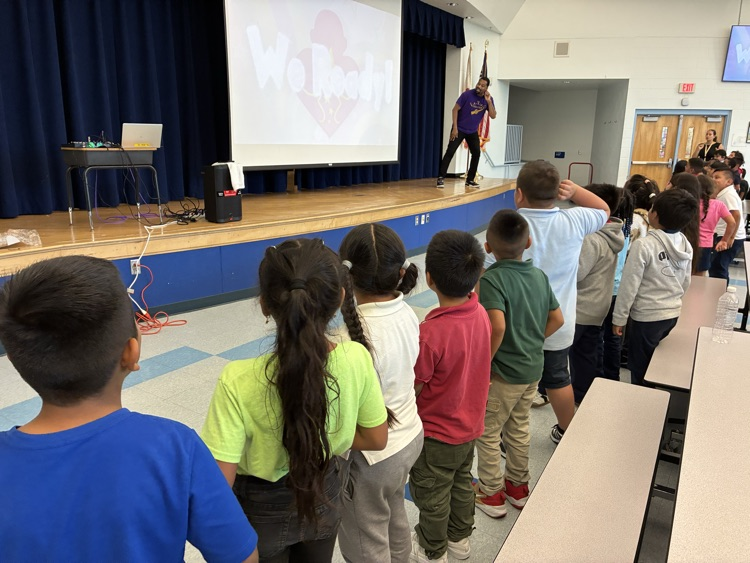 a man leans on stage into a cafeteria filled with students 