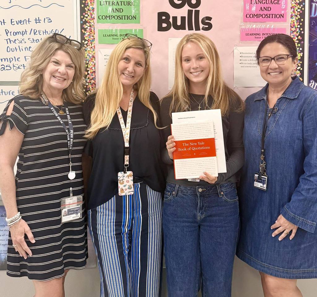 A group of women smiling while surrounding a high school student holding a Yale book award. 