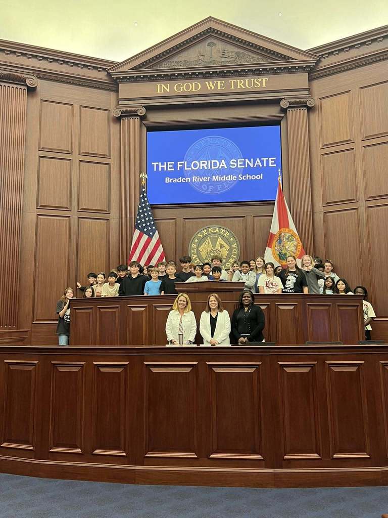 Students and chaperones standing at the state capitol under a sign that reads the name of their school.