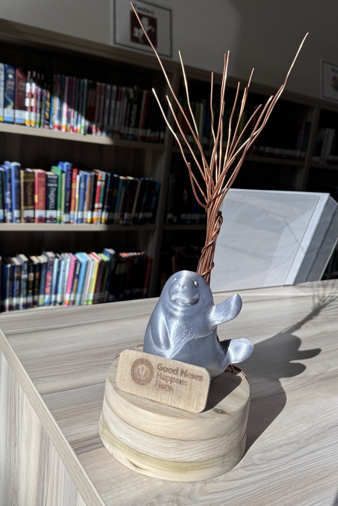 A student-created trophy with a wooden base, a 3-D printed manatee, and a tree twisted with copper pieces.