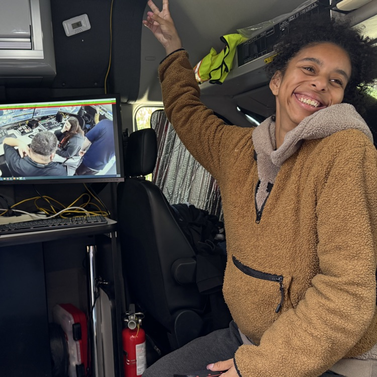 Young woman smiles with holding up a peace sign while sitting in a television live truck