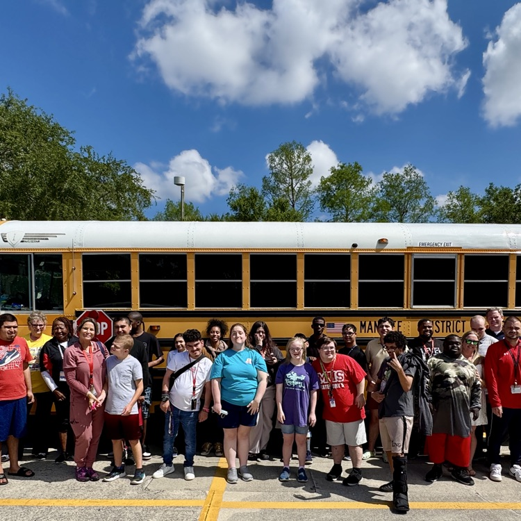 students, teachers and staff stand in front of a school bus during a field trip