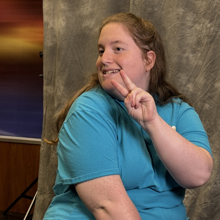 A young woman holds up a peace sign while getting her portrait taken on a field trip
