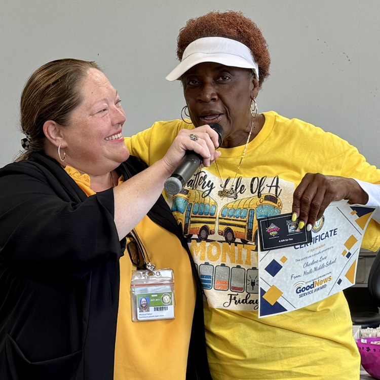 A transportation employee holding a certificate and wearing a yellow T-shirt, speaking into a microphone