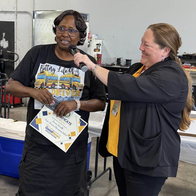A transportation employee wearing a black T-shirt based into the microphone while holding a certificate
