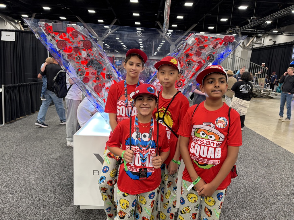 Kids wearing Sesame Street hats, shirts, and pants, stand in front of a lighted sculpture.