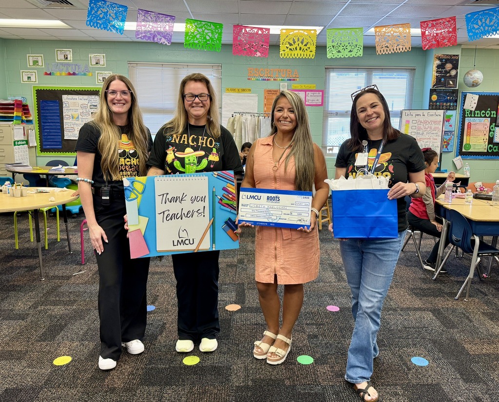 School administrators and a teacher smiling while standing in a bright decorated classroom.