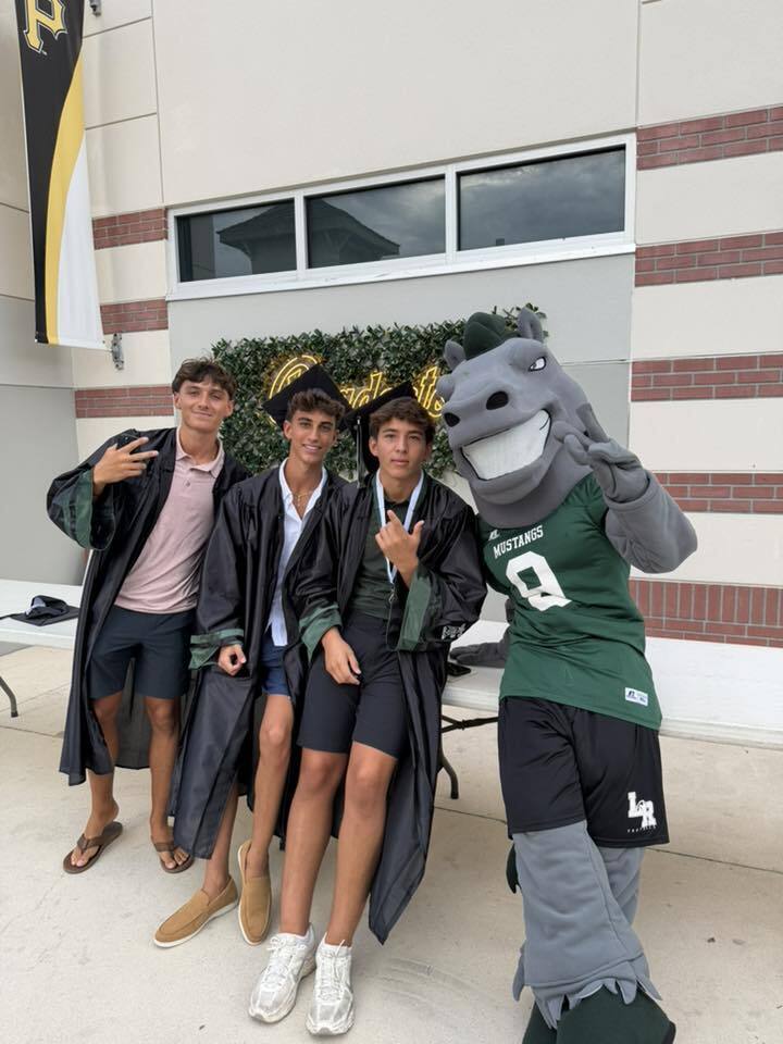 Three young men in black graduation gowns with the mustang horse mascot.