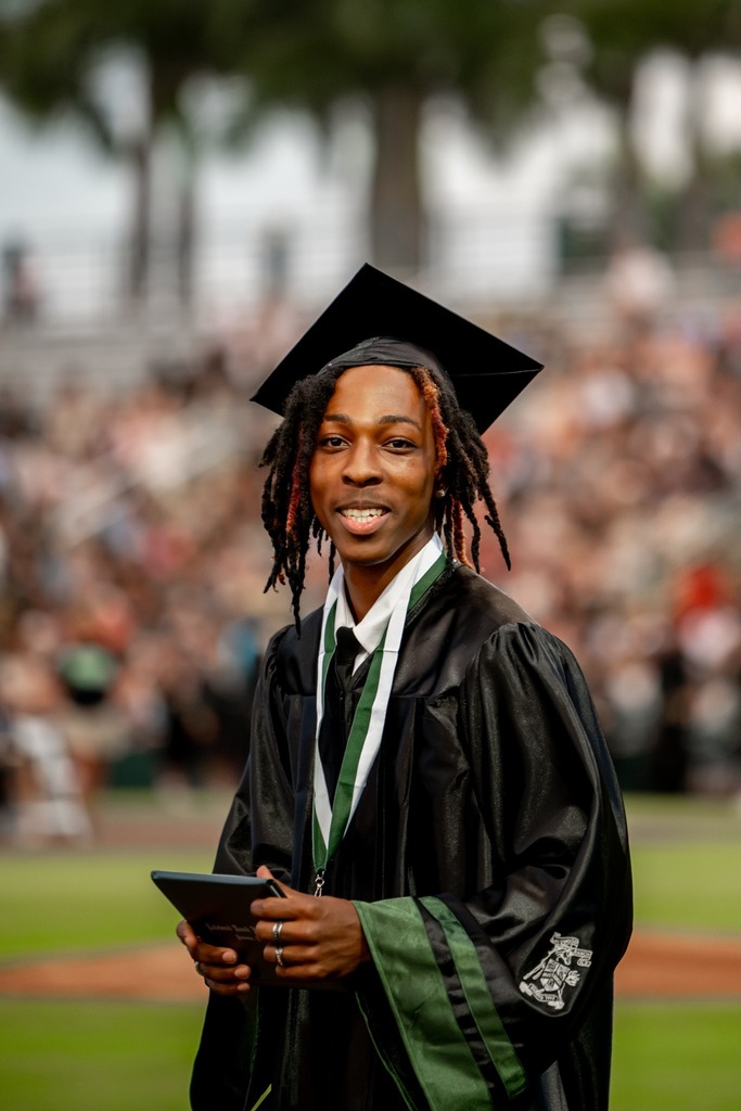 A graduate holding a diploma and wearing a black gown.