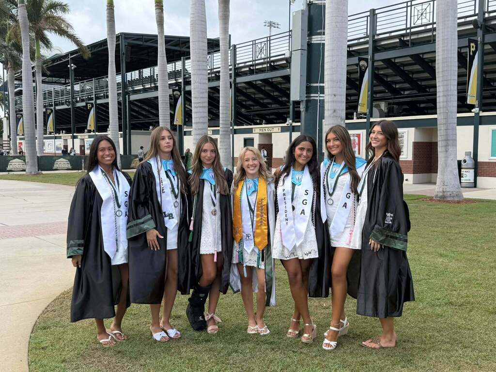 A group of female high school graduates with arms around one another before the ceremony.