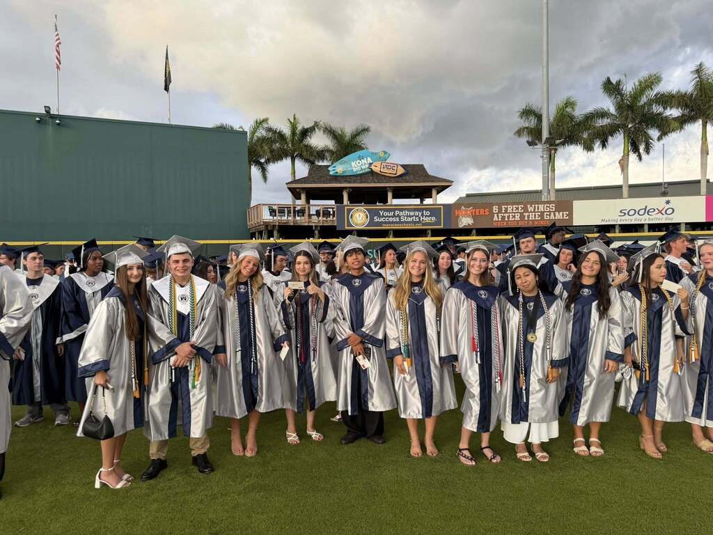 A line of graduates smiling in silver gowns.