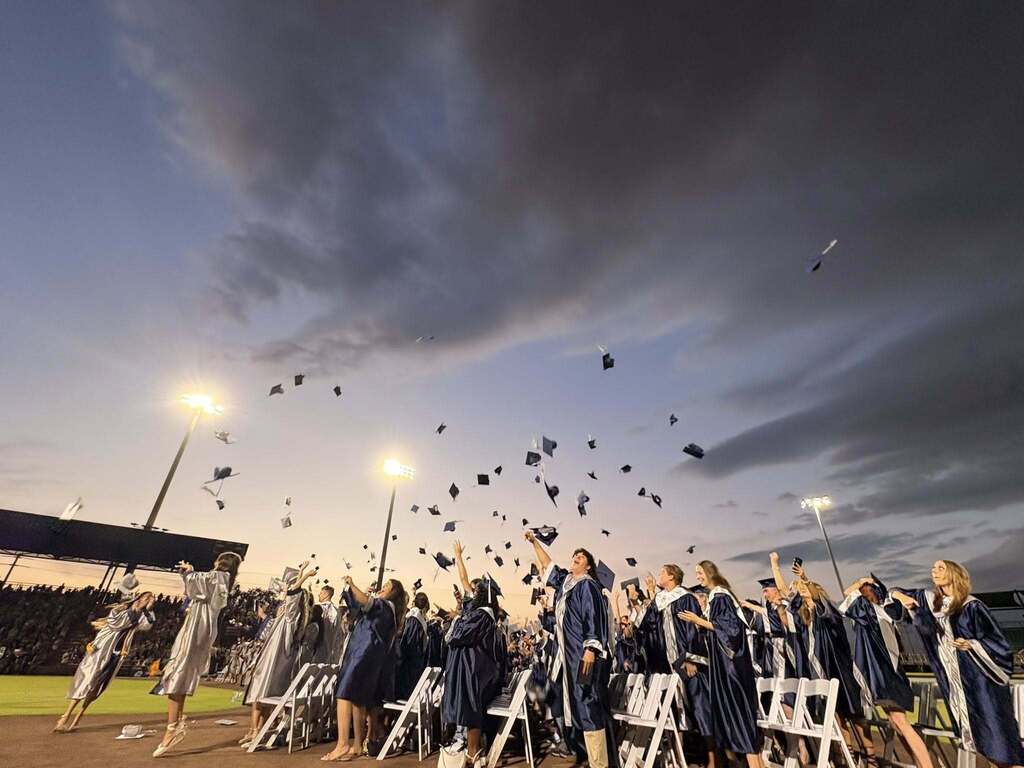 The scene as high school graduates toss their caps in the air and greyish clouds loom over them.