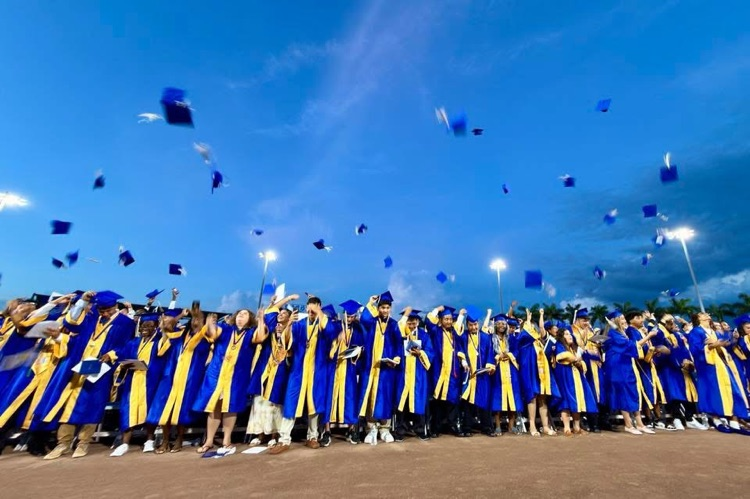 graduates in blue gowns throw their caps into the air