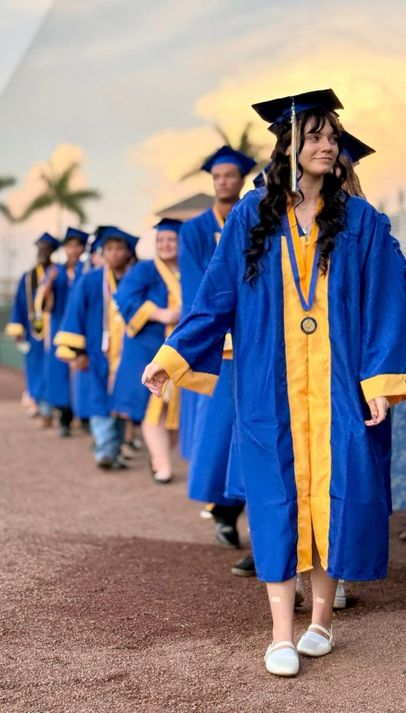 High school graduates in blue and gold gowns lineup to receive their diploma