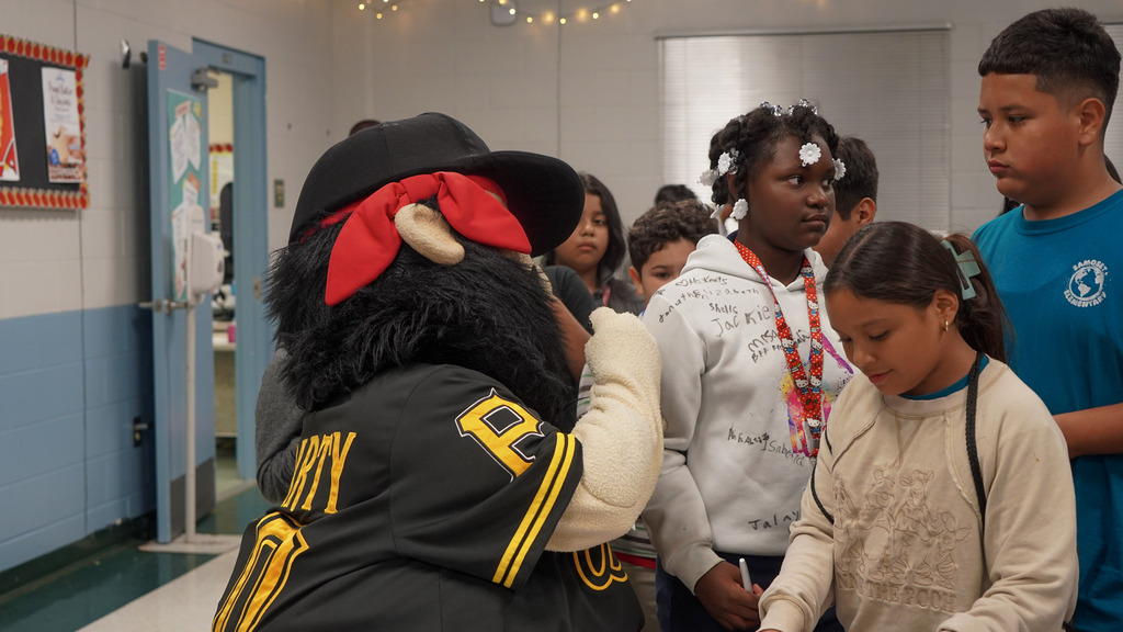 A pirate mascot writes on a young girl's white sweatshirt with a sharpie marker.