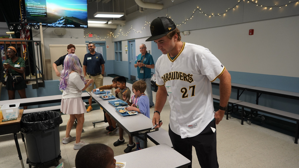 A baseball player holding a sharpie looking down at a young boy.