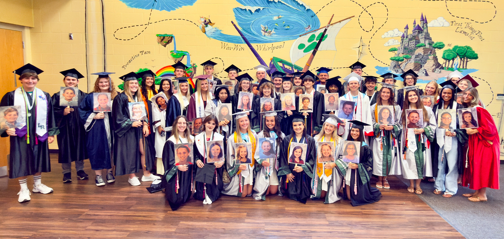 A group of high school graduates holding their photos from elementary school.