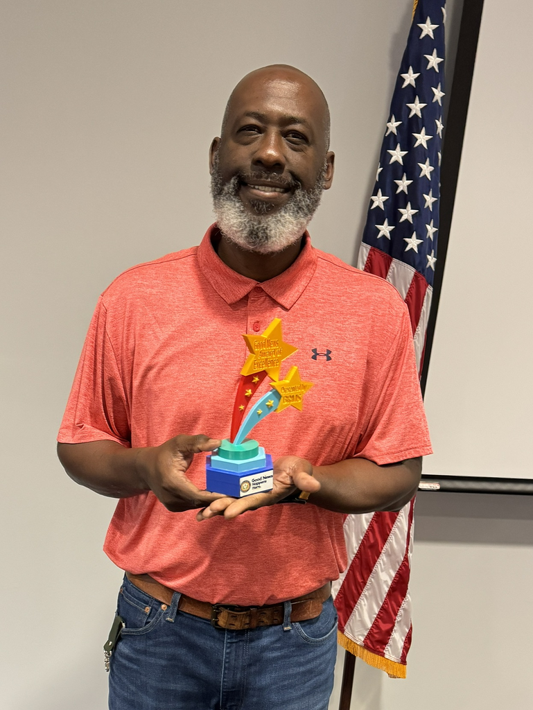 A man in an orange polo shirt holds a student-created trophy with brightly colored stars. 