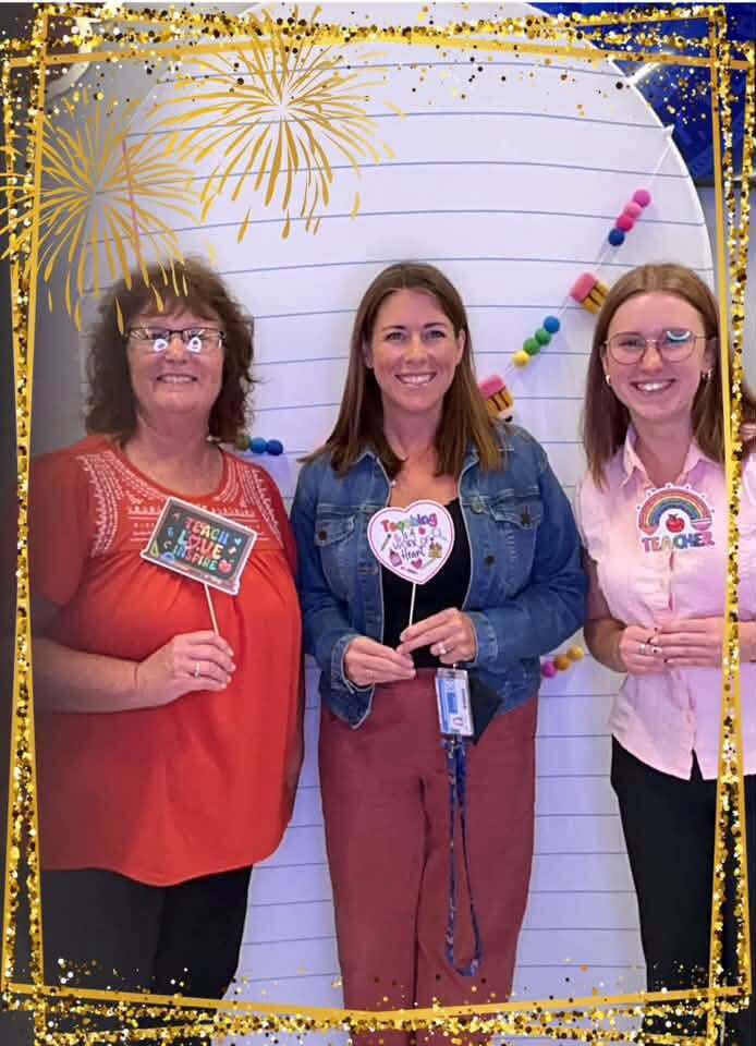 Three smiling women holding signs in a photo booth
