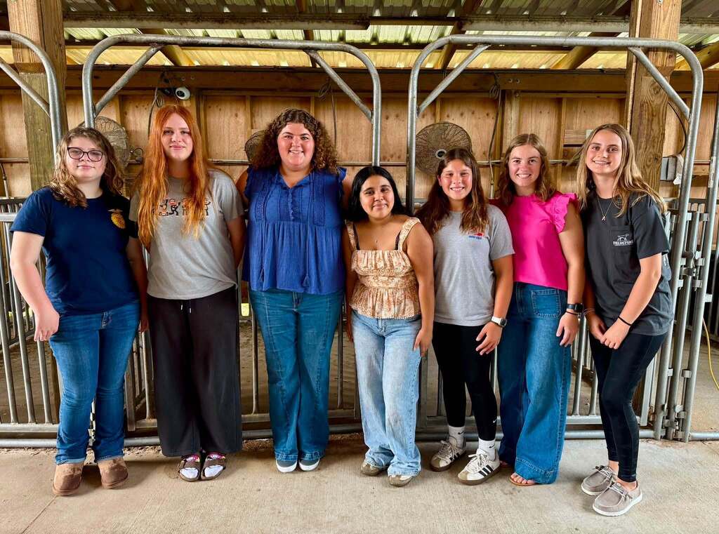 Students and their teachers smiling while standing in a middle school agriculture barn.