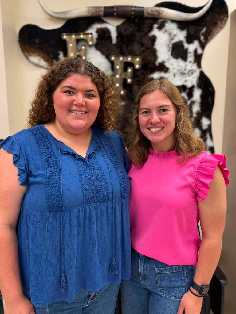 New teachers smiling in a classroom with a light up FFA sign behind them.